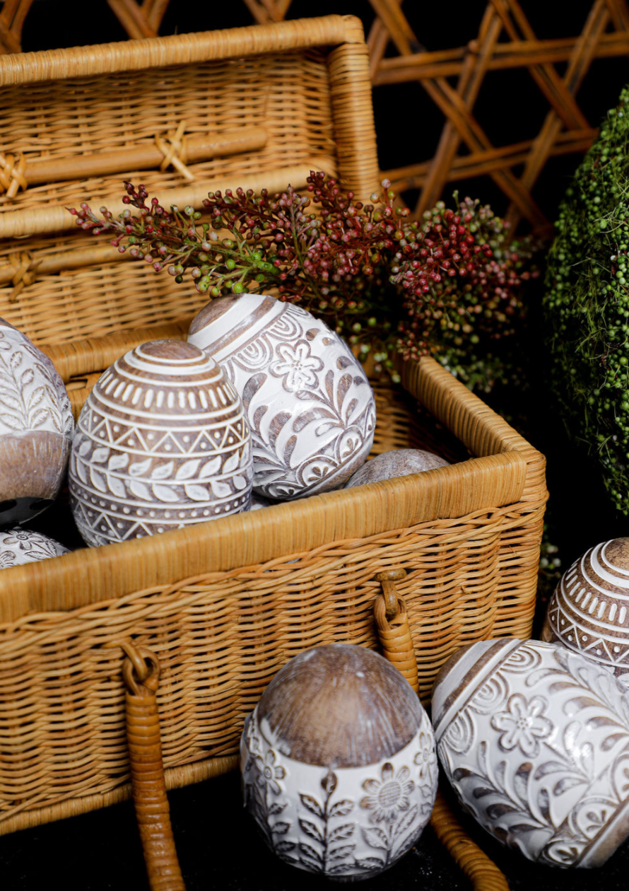Whitewashed floral resin Easter egg with carved designs, in a woven basket with decorative foliage.
