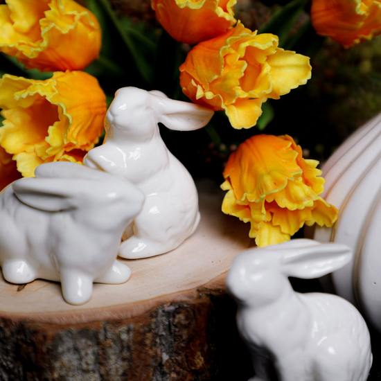 Assorted white porcelain bunnies for home decor with yellow flowers on a wood slice.