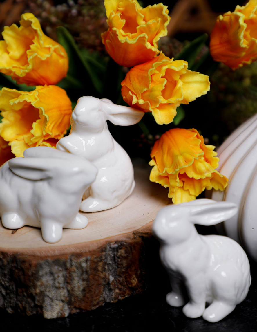 Assorted white porcelain bunnies for home decor with yellow flowers on a wood slice.