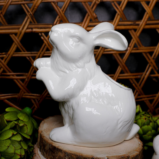 White ceramic Easter bunny vase from Park Designs atop a wood slice and surrounded by artichokes.
