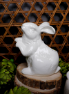 White ceramic Easter bunny vase from Park Designs atop a wood slice and surrounded by artichokes.
