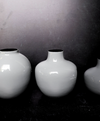 Three white vases of different sizes on a dark surface with a gray background