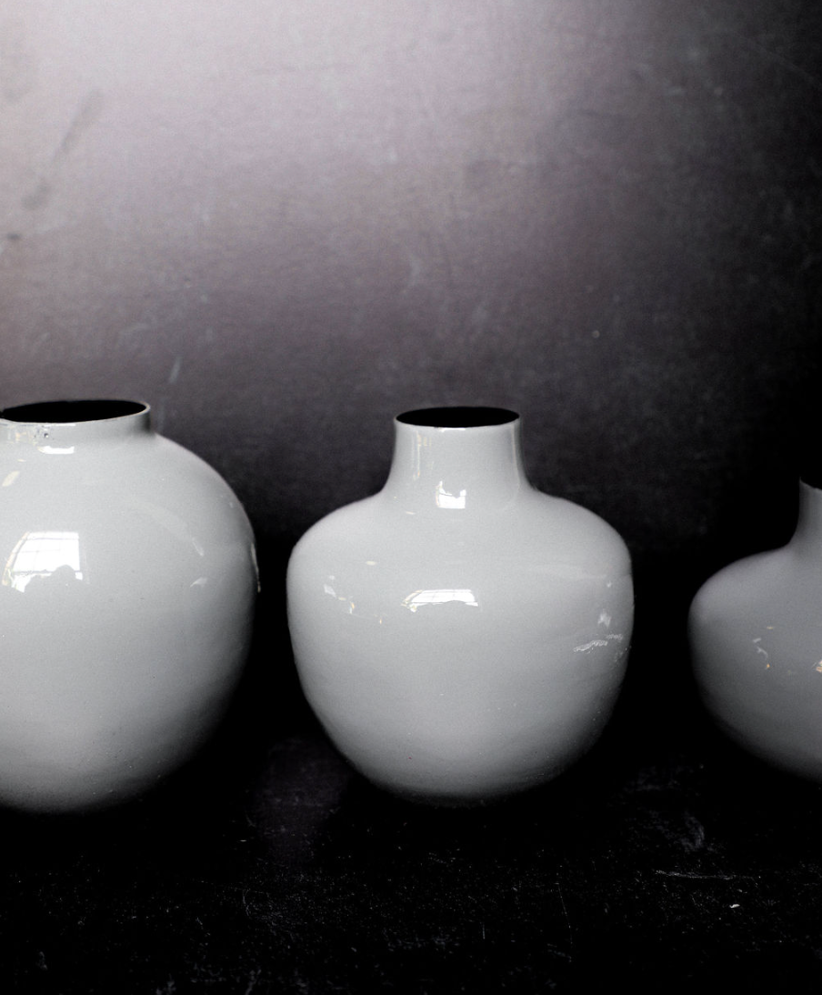 Three white vases of different sizes on a dark surface with a gray background