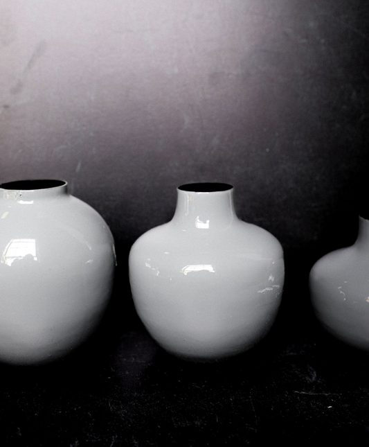 Three white vases of different sizes on a dark surface with a gray background