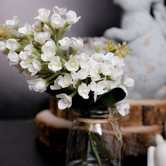 Small glass vase with white flowers on a dark surface with a blurred background