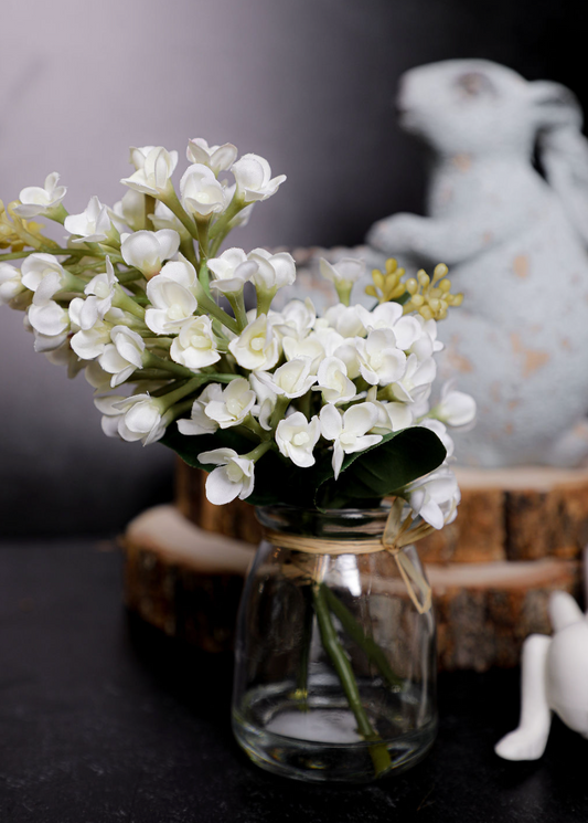 Small glass vase with white flowers on a dark surface with a blurred background