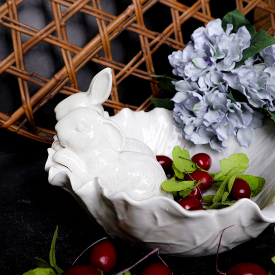 Decorative white bowl with floral and fruit arrangement on a dark background
