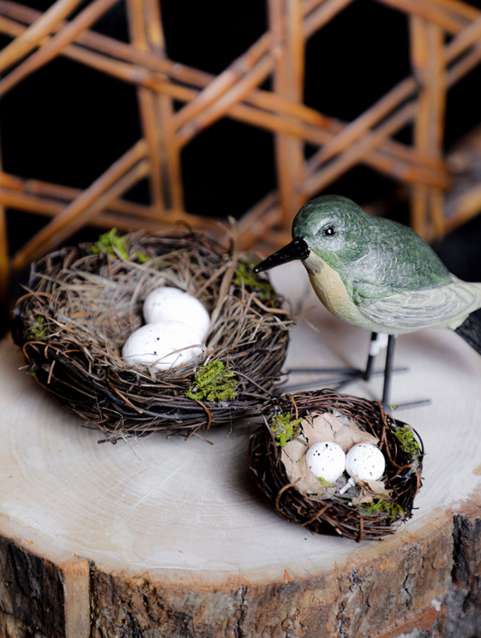 Decorative scene with bird figurine, nests, and eggs on a wooden surface.