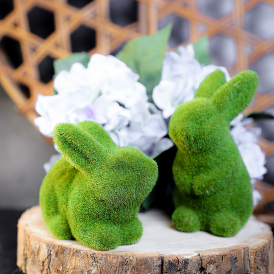 Green flocked bunny home decor item with mossy texture, on a wood slice with floral arrangement.
