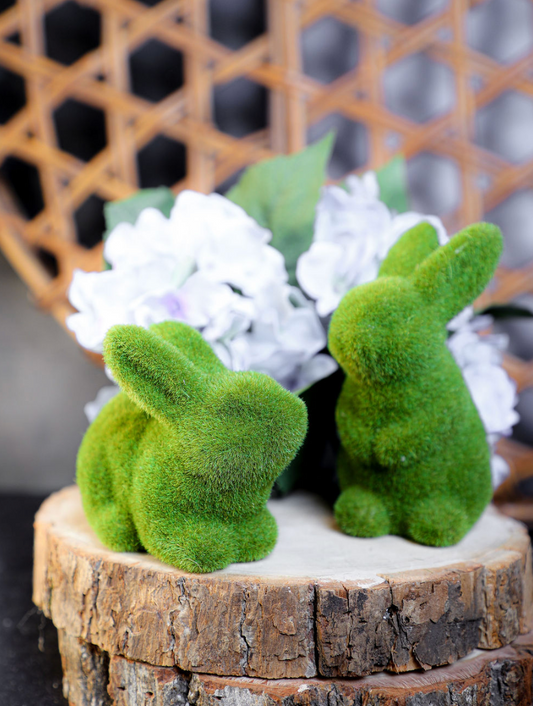 Green flocked bunny home decor item with mossy texture, on a wood slice with floral arrangement.
