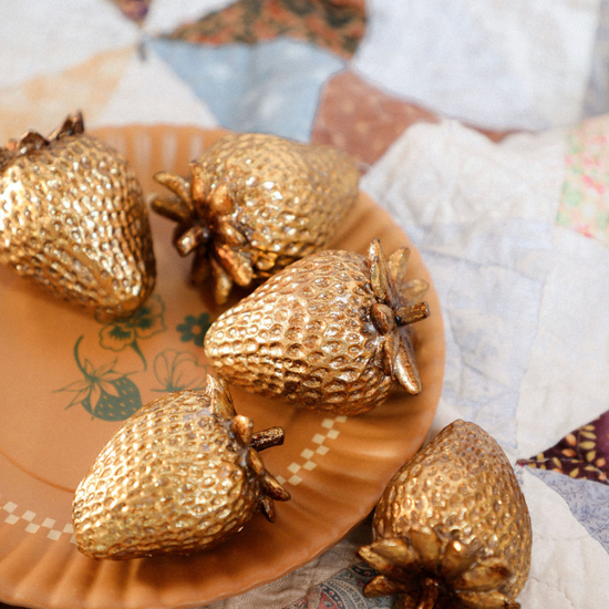 Gold strawberry-shaped objects on a decorative plate with a patchwork quilt background