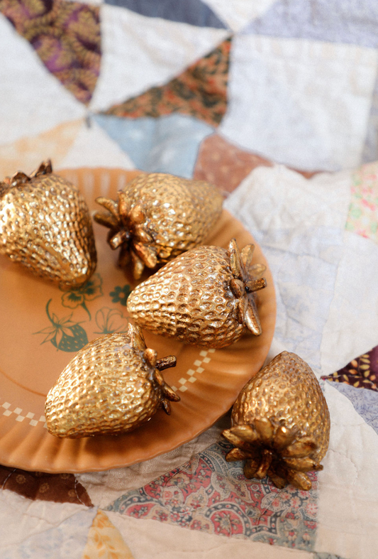 Gold strawberry-shaped objects on a decorative plate with a patchwork quilt background