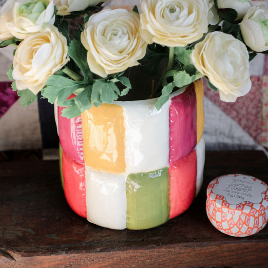 Colorful patchwork vase with white flowers on a wooden surface