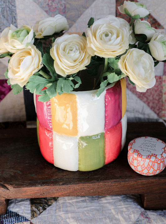 Colorful patchwork vase with white flowers on a wooden surface