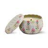 Floral patterned tin candle by Paddywax with its lid leaning open, revealing its lit wick.