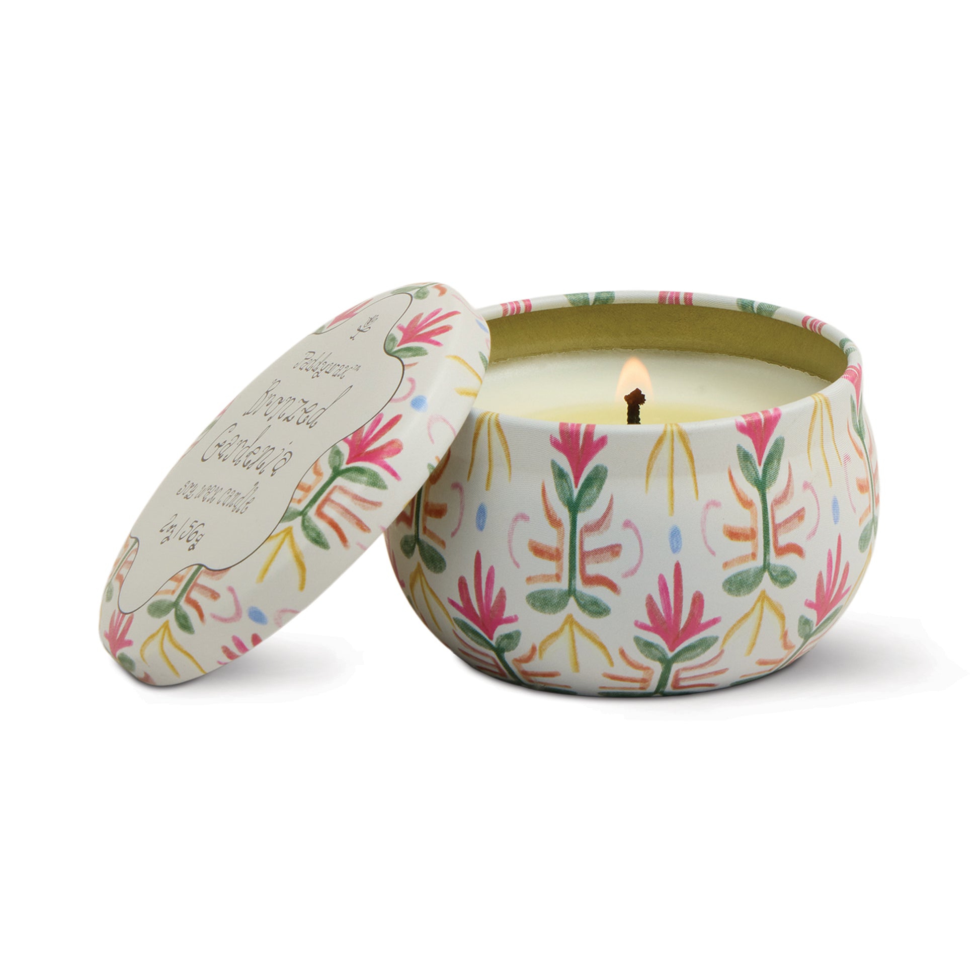Floral patterned tin candle by Paddywax with its lid leaning open, revealing its lit wick.
