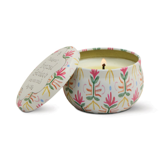 Floral patterned tin candle by Paddywax with its lid leaning open, revealing its lit wick.