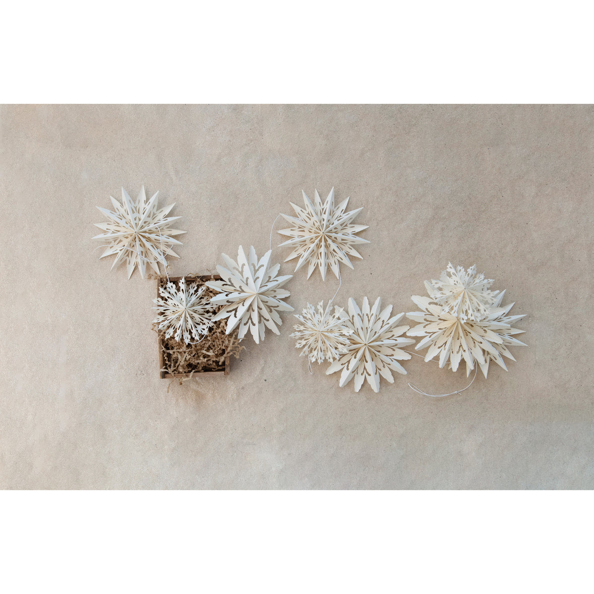 72-inch long snowflake garland with string, arranged with brown paper shreds in a square wooden box.