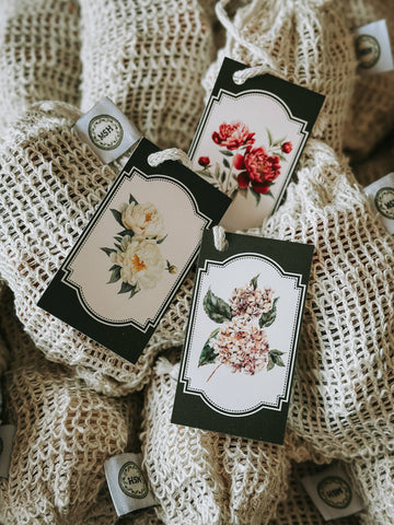 Mesh soap scrubs with floral hang tags, featuring decorative logo tags.