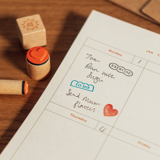 Planner page with stamps and handwritten notes, including a heart stamp, next to wooden stamps.
