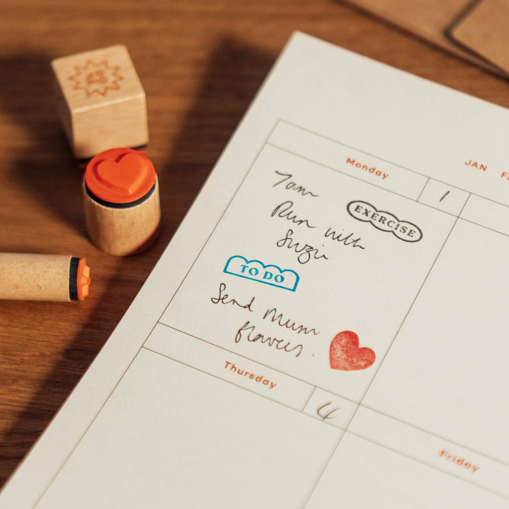 Planner page with stamps and handwritten notes, including a heart stamp, next to wooden stamps.
