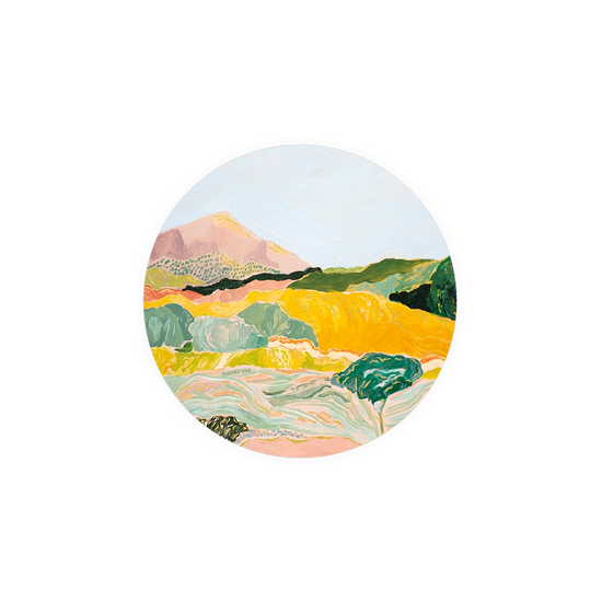 Round landscape art coaster by Margaret Teake, featuring yellow fields, a mountain, and stylized trees.
