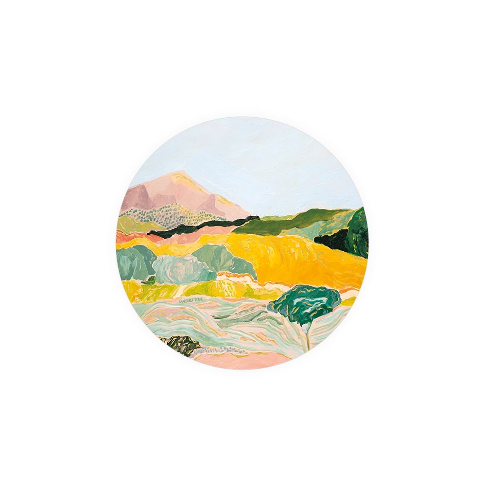 Round landscape art coaster by Margaret Teake, featuring yellow fields, a mountain, and stylized trees.
